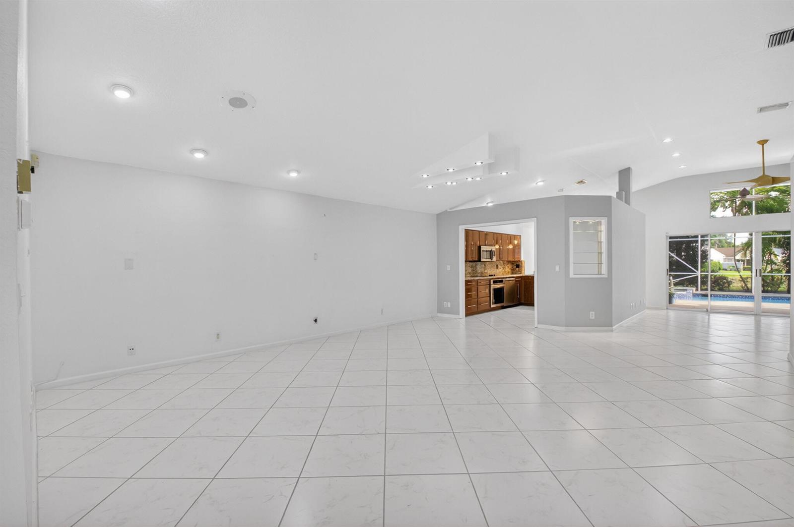 A spacious, open-concept living area features white tiled floors, recessed lighting, and a kitchen view — 7558 Ironbridge Circle, Delray Beach FL 33446, DELRAY BEACH, FL