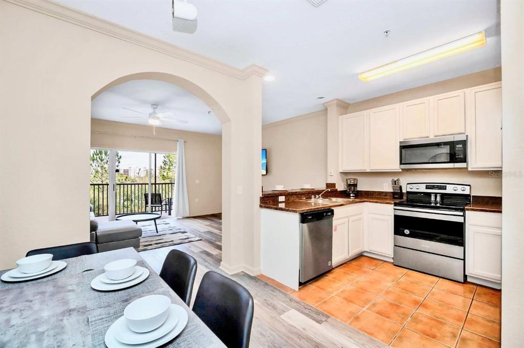 A kitchen with white cabinets and stainless steel appliances overlooks a dining area and balcony — 14200 AVALON ROAD UNIT 426, WINTER GARDEN, FL