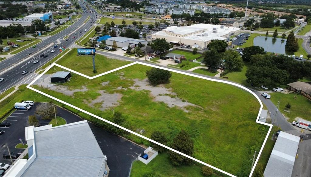 An aerial view shows a vacant, grassy commercial lot outlined in white near a highway — BROADVIEW DRIVE, KISSIMMEE, FL