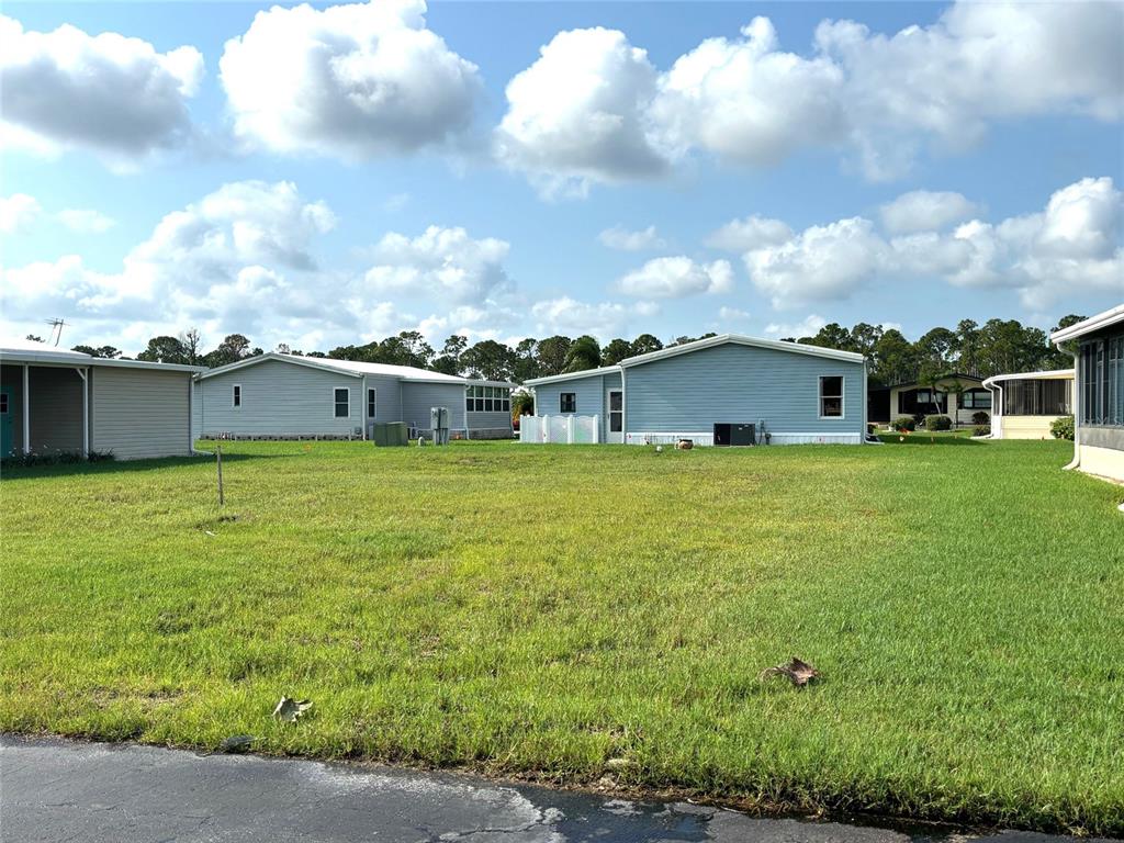 A grassy vacant lot sits between several light-colored manufactured homes under a cloudy sky — 705 DEL LUNA DRIVE, NORTH PORT, FL