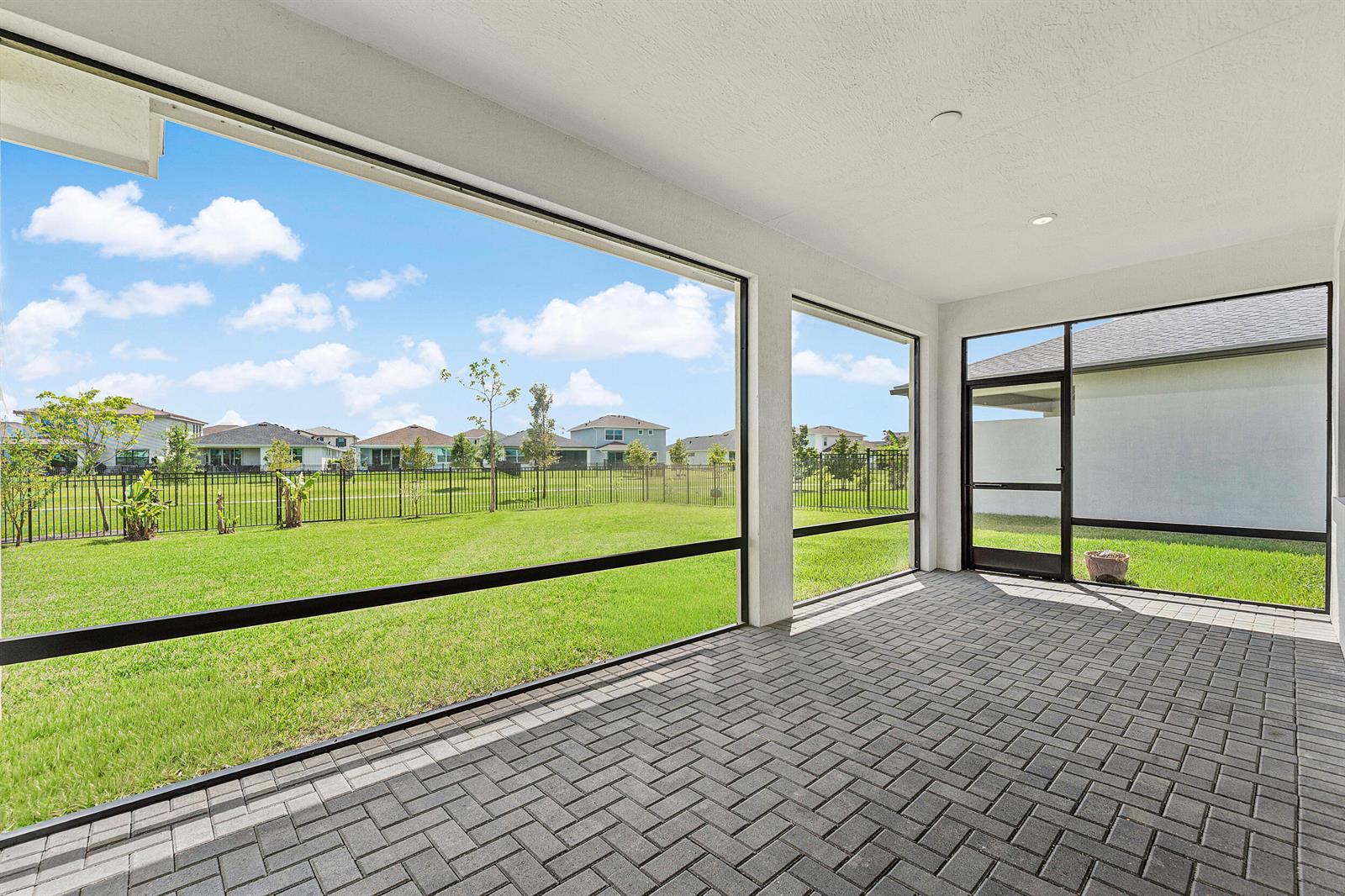 A covered patio with brick pavers and screen walls overlooks a fenced backyard and neighborhood — 1887 Wandering Willow Way, Loxahatchee FL 33470, LOXAHATCHEE, FL