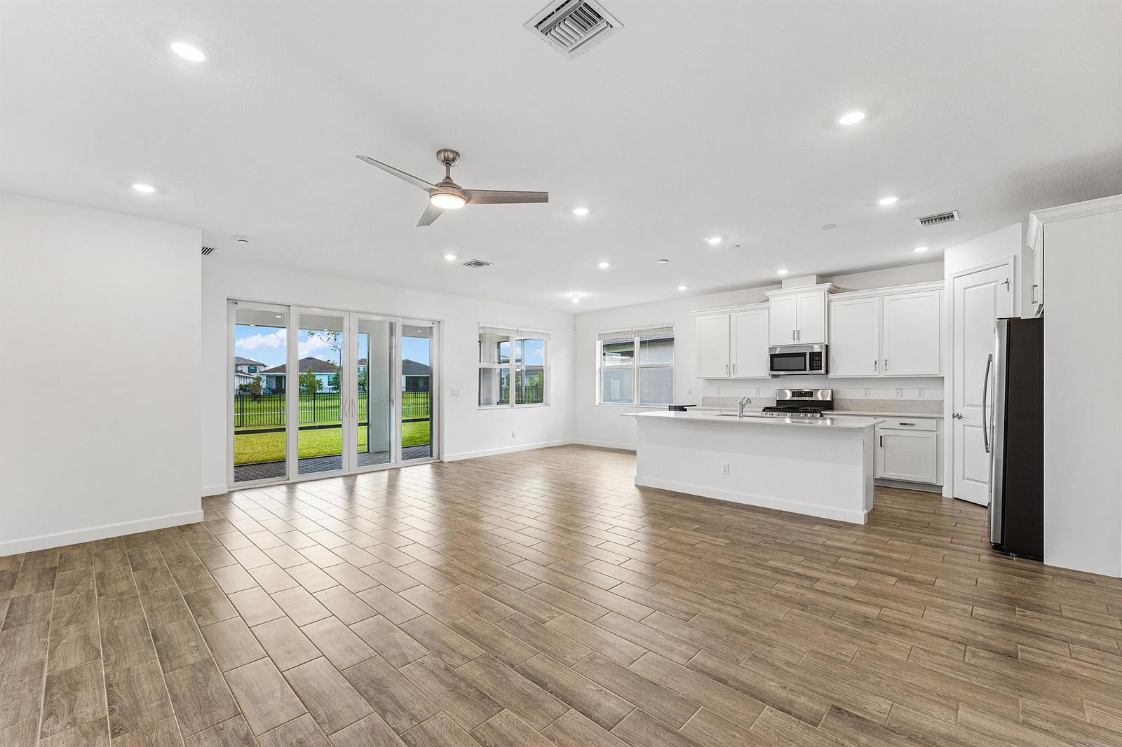 An open-concept kitchen and living area features white cabinetry, a kitchen island, and tile flooring — 1887 Wandering Willow Way, Loxahatchee FL 33470, LOXAHATCHEE, FL