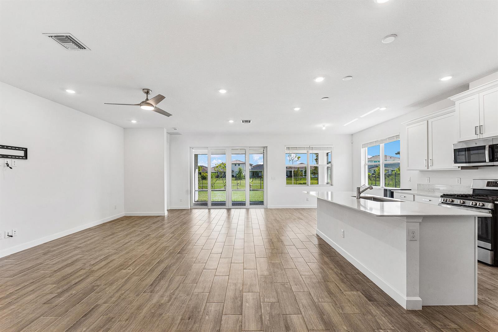 An open-concept kitchen and living area features white cabinetry, quartz countertops, and wood-look tile flooring — 1887 Wandering Willow Way, Loxahatchee FL 33470, LOXAHATCHEE, FL