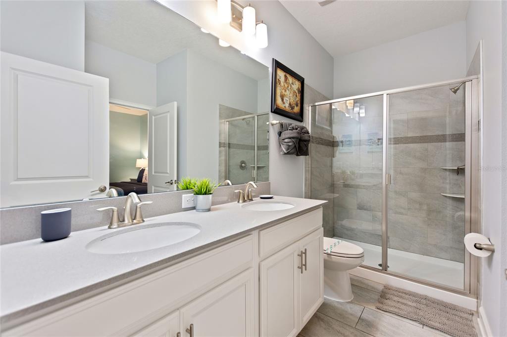 A bathroom features a double vanity with white cabinets, a mirror, and a glass shower — 1594 SANDBAGGER DRIVE, DAVENPORT, FL