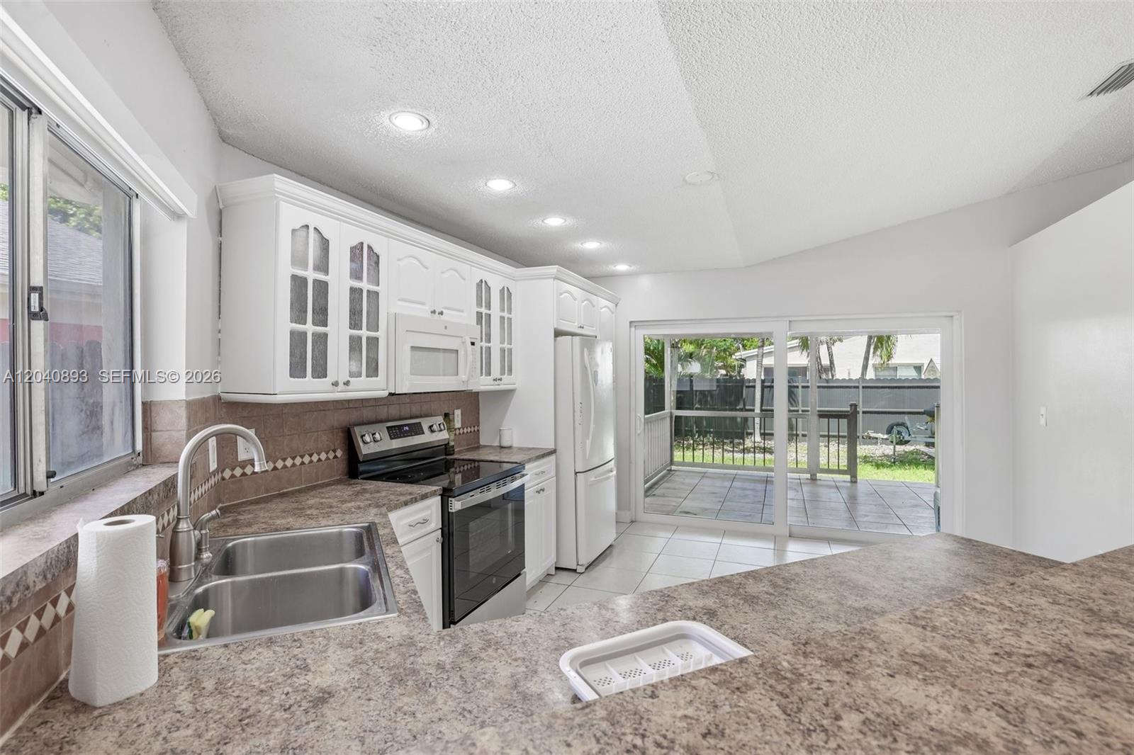 A kitchen features white cabinets, laminate countertops, a double sink, and a sliding glass door — 9709 SW 146th Ct, Miami FL 33186, MIAMI, FL