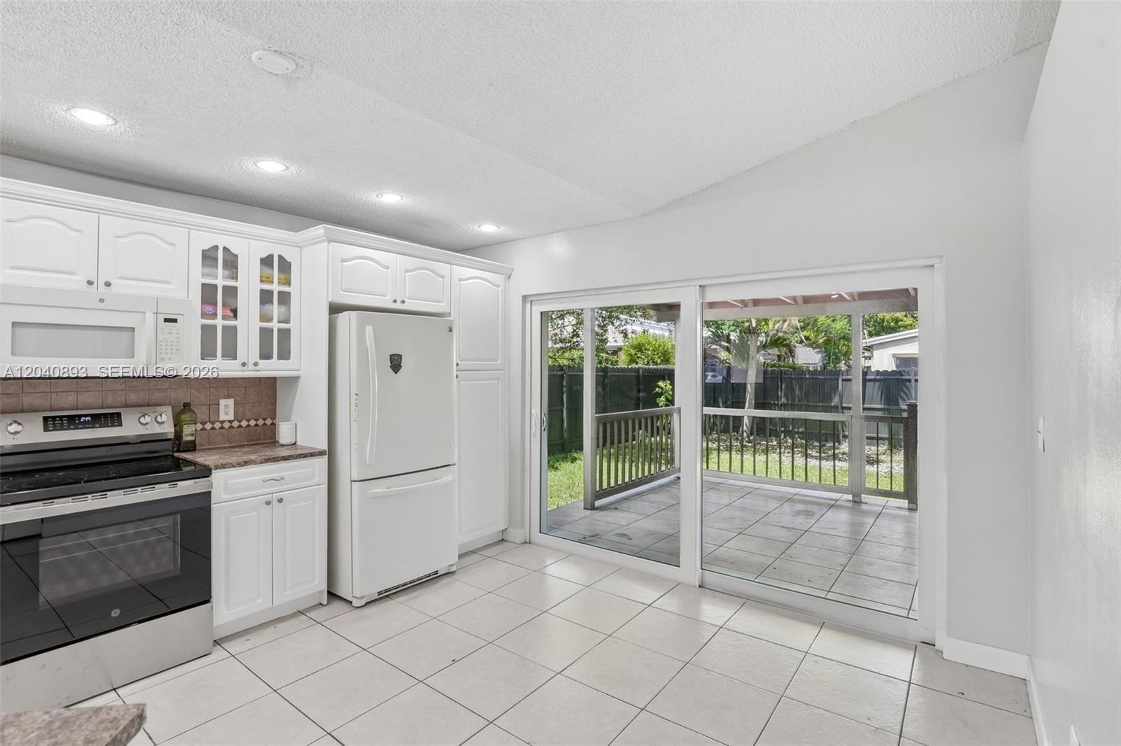 A kitchen with white cabinets, a white refrigerator, and a sliding glass door to a patio — 9709 SW 146th Ct, Miami FL 33186, MIAMI, FL