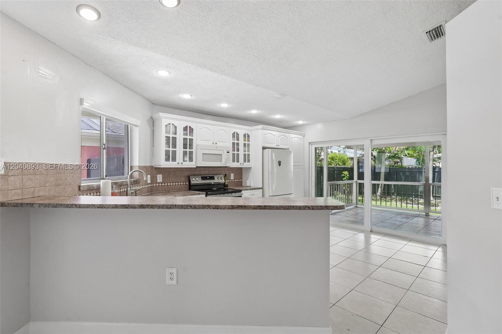 A kitchen with white cabinets, a breakfast bar, and sliding glass doors to a patio — 9709 SW 146th Ct, Miami FL 33186, MIAMI, FL