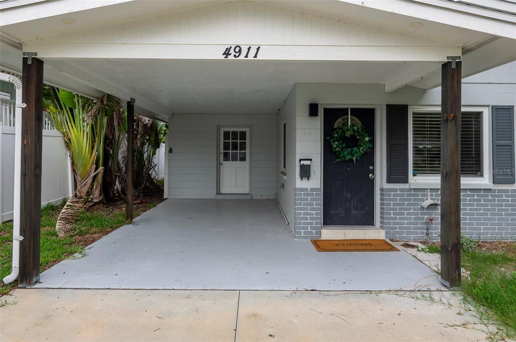 A covered carport leads to a black front door with a wreath and a welcome mat — 4911 CHANCELLOR STREET NE, ST PETERSBURG, FL
