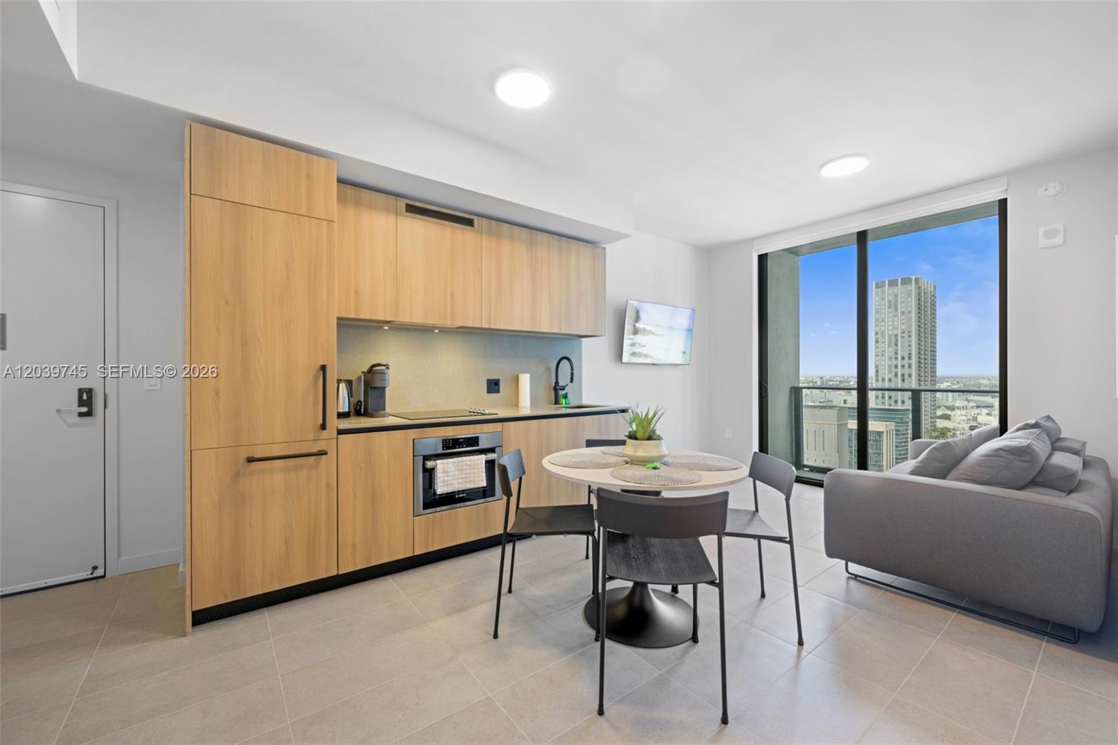 A modern studio apartment features a kitchenette with light wood cabinets and a city view — 121 NE 5th St # 3006, Miami FL 33132, MIAMI, FL