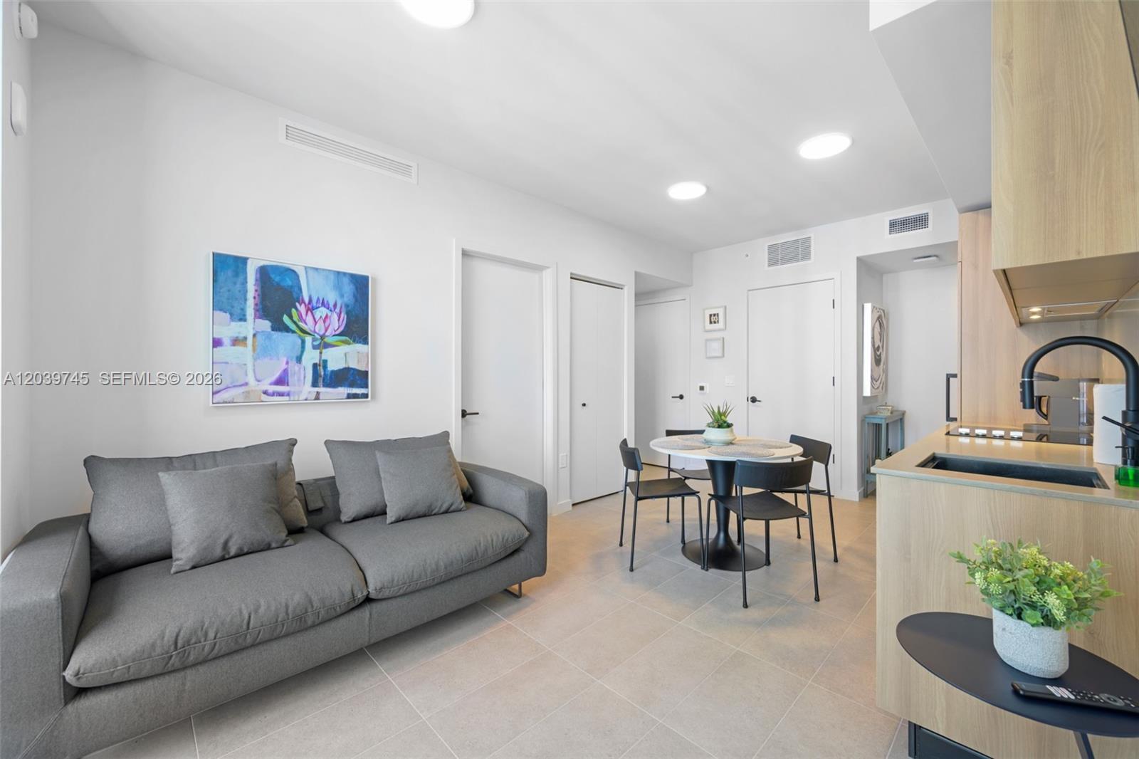 A modern studio apartment features a gray sofa, a small dining table, and a kitchenette — 121 NE 5th St # 3006, Miami FL 33132, MIAMI, FL