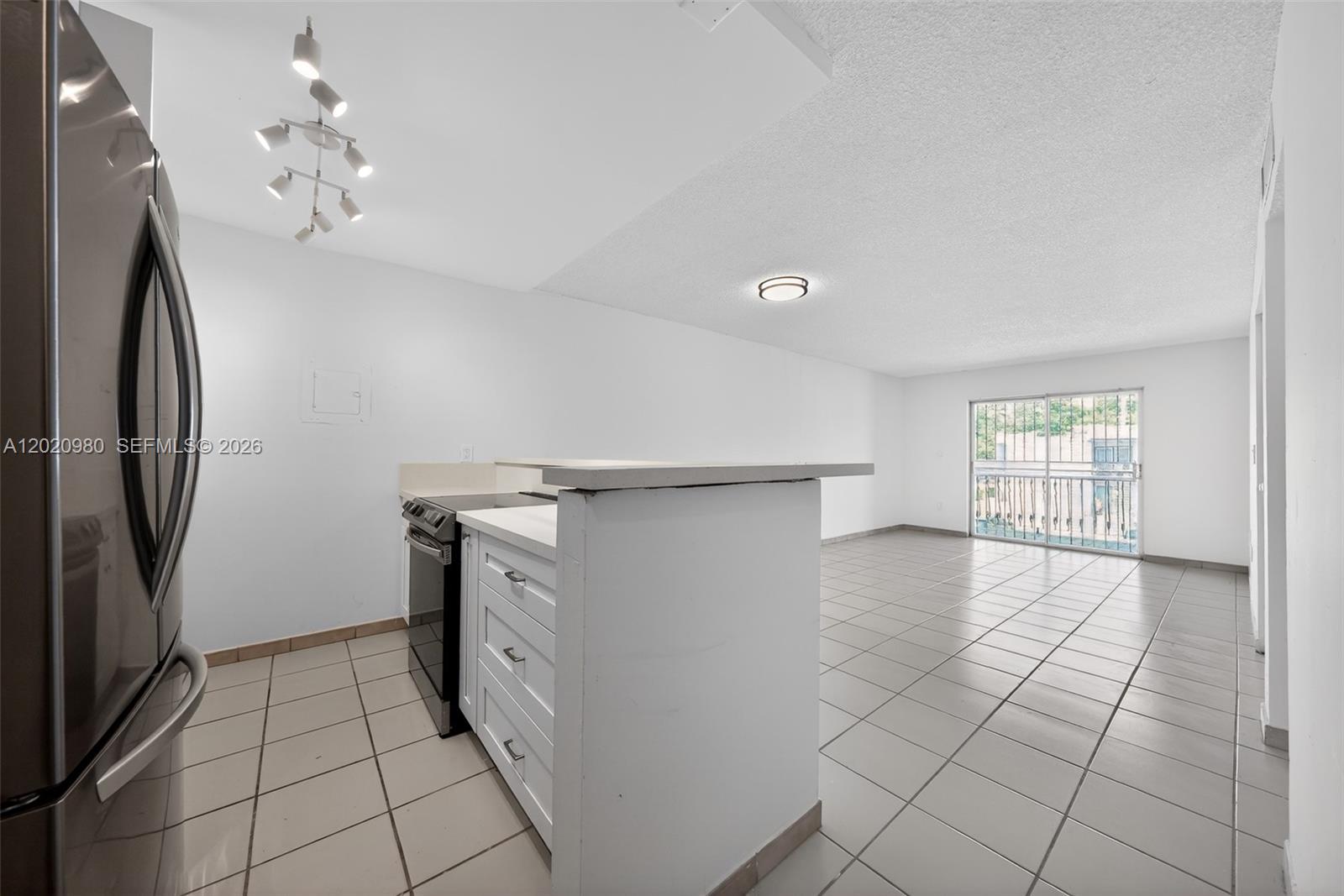 A kitchen with white cabinets and a breakfast bar opens into a tiled living area — 145 SW 30TH CT # B208, Miami FL 33135, MIAMI, FL