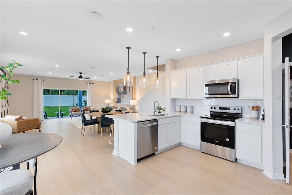 A modern kitchen with white cabinets and stainless steel appliances opens to a living area — 472 BERYL COVE, SANFORD, FL