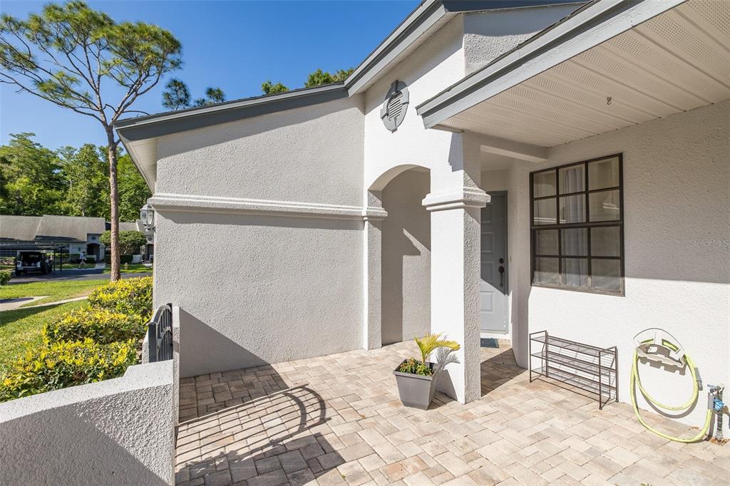A paved entryway leads to a gray front door under a covered porch — 3843 GOLDFINCH COURT, PALM HARBOR, FL