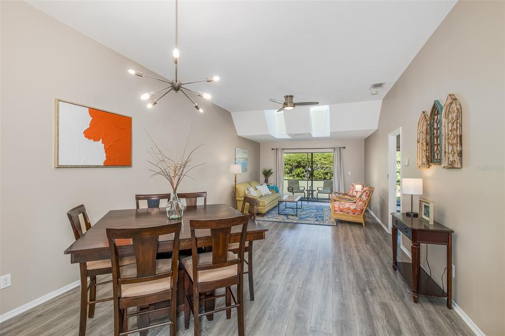 A dining area and living room with wood-look flooring, vaulted ceilings, and a sliding glass door — 3843 GOLDFINCH COURT, PALM HARBOR, FL