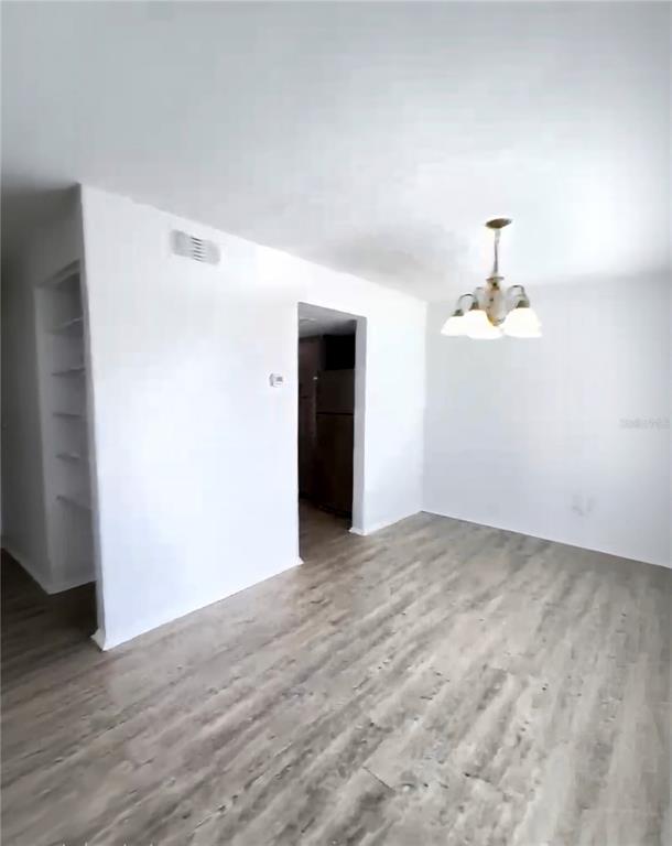 An empty room with light wood-look flooring, white walls, a chandelier, and an open doorway — 3982 CRAYRICH CIRCLE UNIT C4, ORLANDO, FL