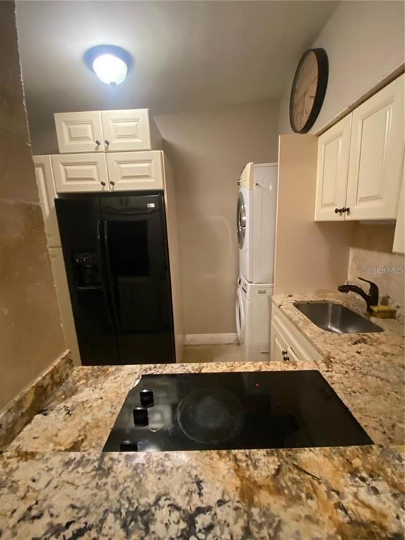 A kitchen features a black refrigerator, stacked laundry unit, granite countertops, and white cabinetry — 270 110TH AVENUE, TREASURE ISLAND, FL