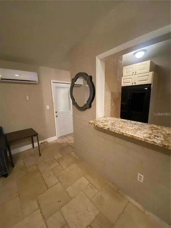 A room with stone flooring features a breakfast bar, a mirror, and a wall-mounted air conditioner — 270 110TH AVENUE, TREASURE ISLAND, FL