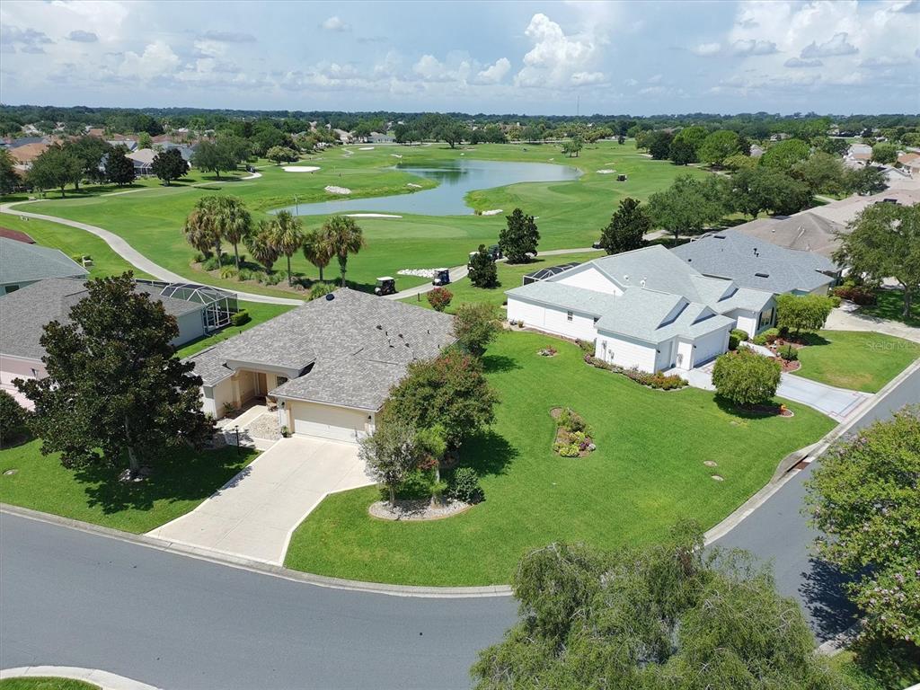 An aerial view shows two houses with gray roofs situated next to a golf course pond — 2314 CALLAWAY DRIVE, THE VILLAGES, FL