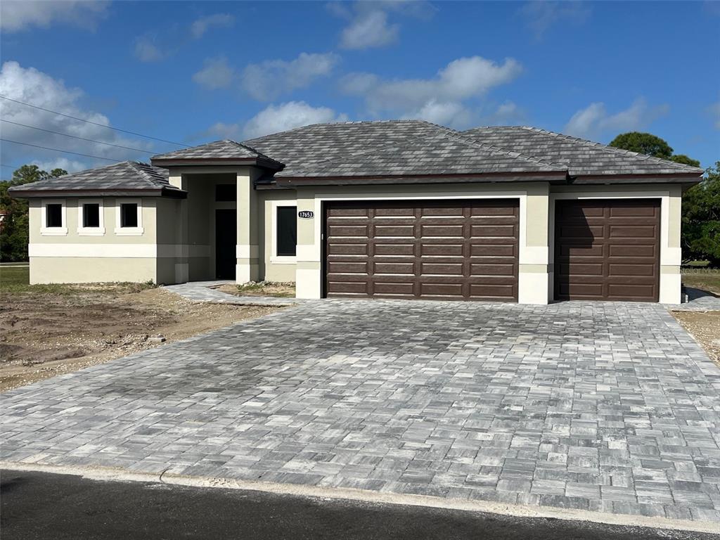 A single-story house with a gray tiled roof, beige stucco walls, and a paved driveway — 17653 VELLUM CIRCLE, PUNTA GORDA, FL