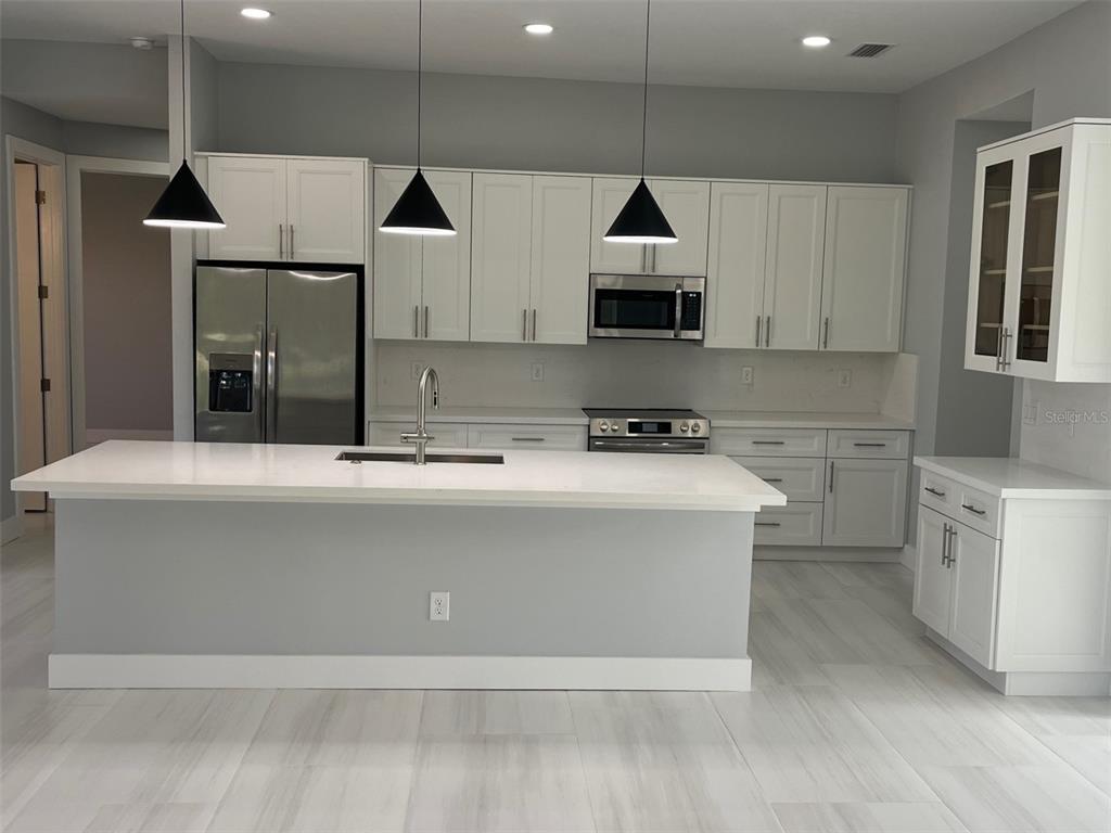 A modern kitchen features white cabinets, a large island with a sink, and stainless appliances — 17653 VELLUM CIRCLE, PUNTA GORDA, FL