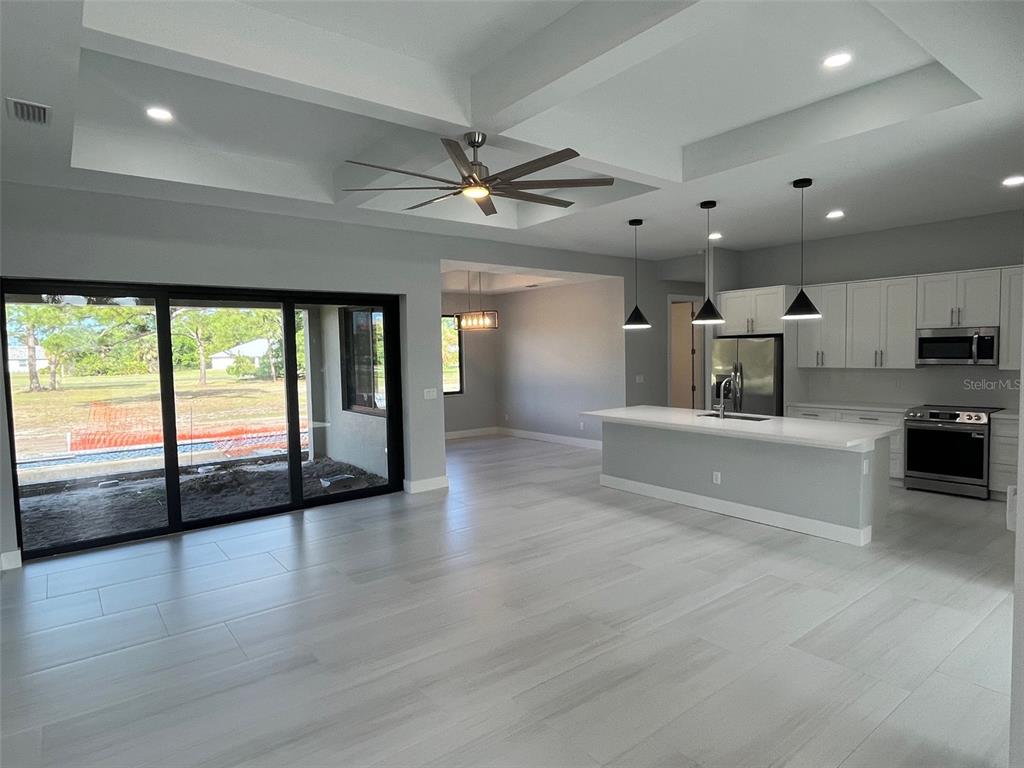 An open-concept kitchen and living area features a tray ceiling, island, and sliding glass doors — 17653 VELLUM CIRCLE, PUNTA GORDA, FL