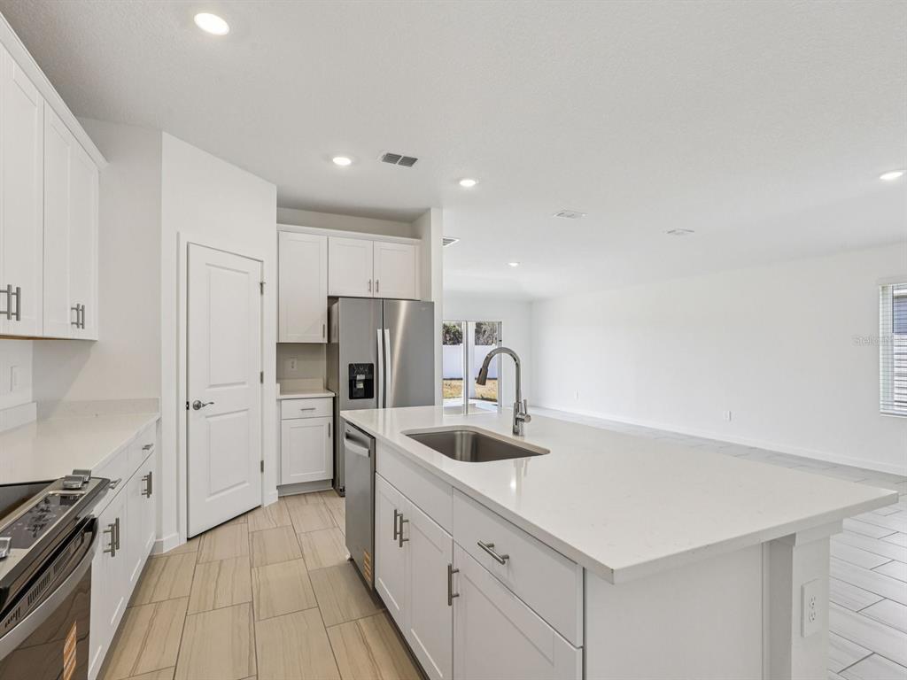A modern kitchen features white cabinets, a large island with a sink, and tile flooring — 34 GARNI DRIVE, PALM COAST, FL