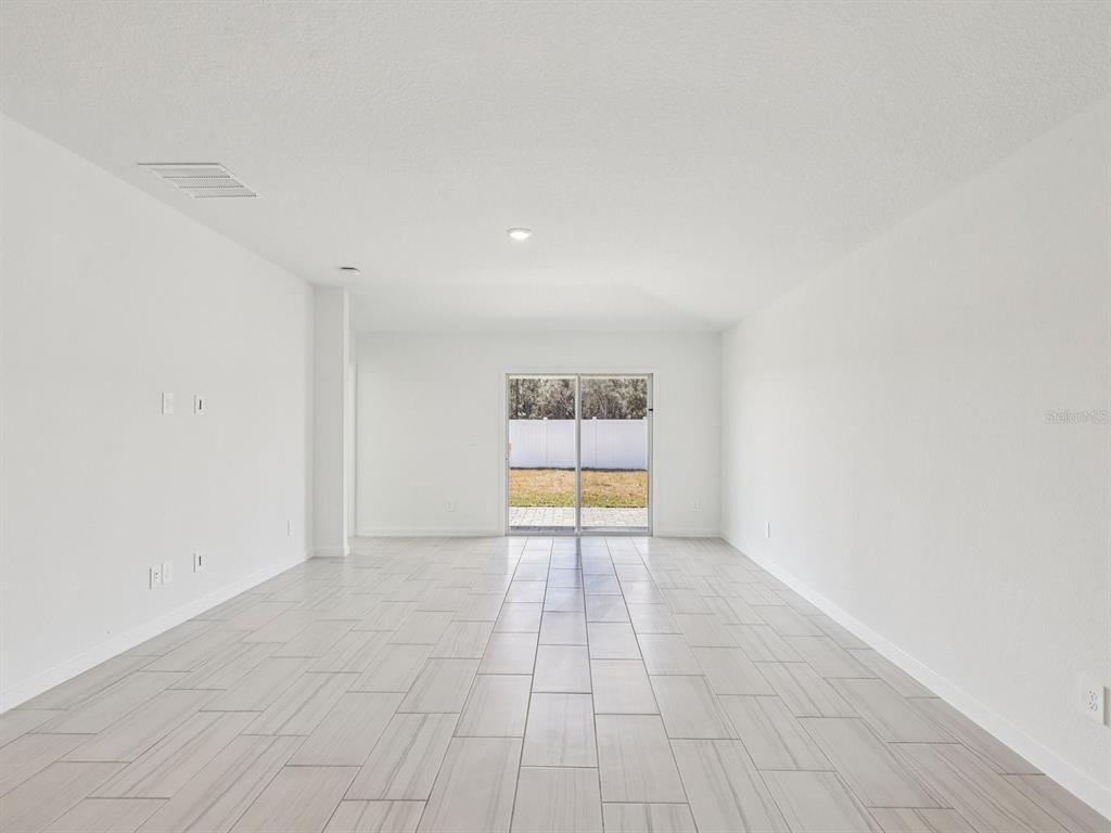 An empty room with white walls, light-colored tile flooring, and a sliding glass door — 34 GARNI DRIVE, PALM COAST, FL