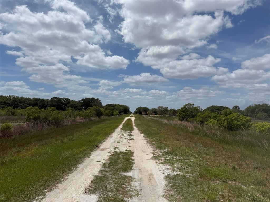 A dirt path stretches through a grassy field under a bright, cloudy sky — 15575 NW 296TH STREET, OKEECHOBEE, FL