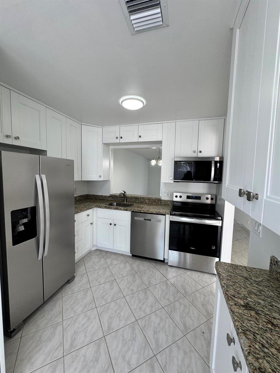 A kitchen features white cabinets, stainless steel appliances, granite countertops, and light tile flooring — 6846 Moonlit Drive, Delray Beach FL 33446, DELRAY BEACH, FL