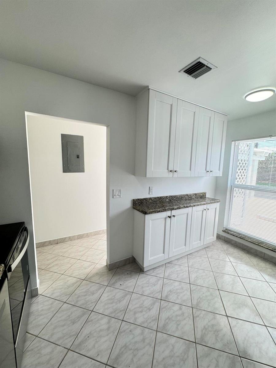 A kitchen area features white cabinets, granite countertops, and light-colored tile flooring — 6846 Moonlit Drive, Delray Beach FL 33446, DELRAY BEACH, FL