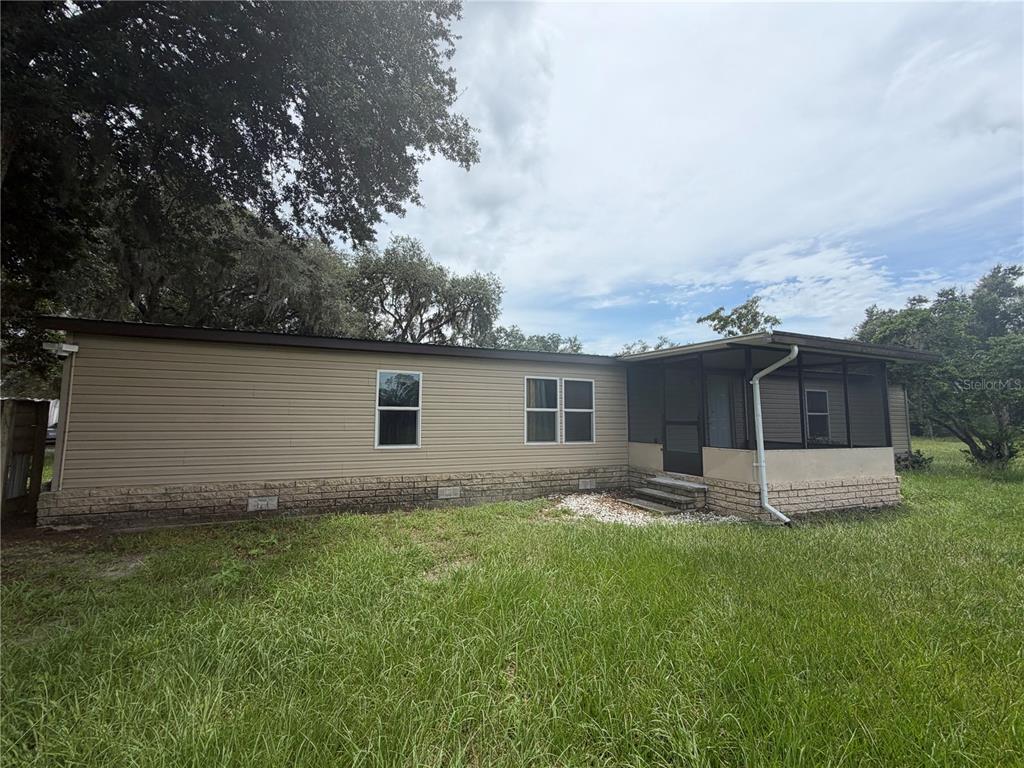 A single-story manufactured home with tan siding, a stone-patterned base, and a screened-in porch — 6828 STATE ROAD 33, CLERMONT, FL