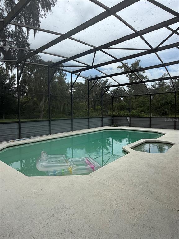 A swimming pool and spa are enclosed within a screened lanai overlooking a wooded area — 6828 STATE ROAD 33, CLERMONT, FL