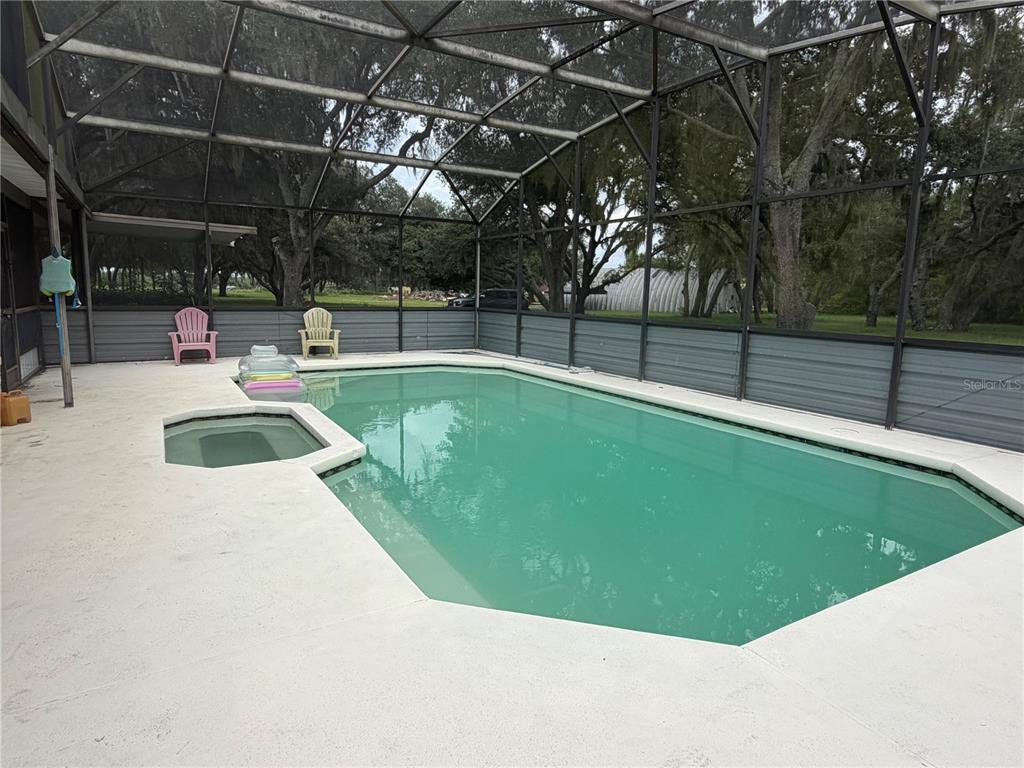A screened-in swimming pool and attached spa sit on a concrete patio with two chairs — 6828 STATE ROAD 33, CLERMONT, FL