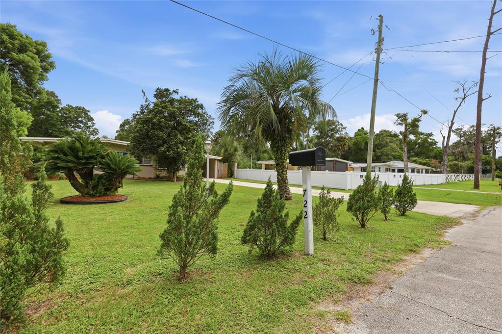 A grassy front yard features a mailbox, several small trees, and a white privacy fence — 722 TEMPLE AVENUE, ORANGE CITY, FL