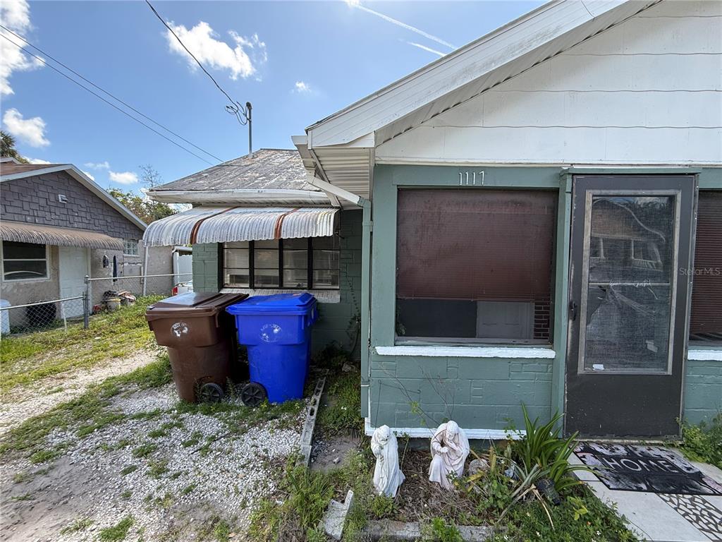 The exterior of a house features green brick walls, a metal awning, and two trash bins — 1117 BRACK STREET, KISSIMMEE, FL