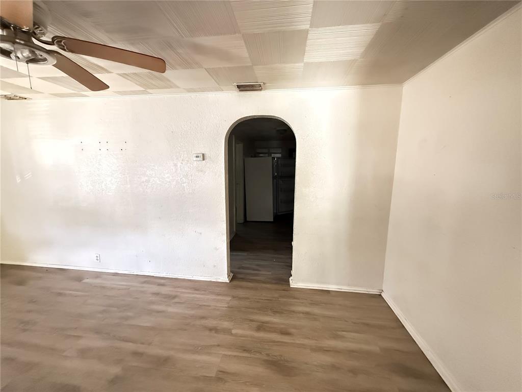A living room with light wood-look flooring, white walls, and an arched doorway to the kitchen — 1117 BRACK STREET, KISSIMMEE, FL