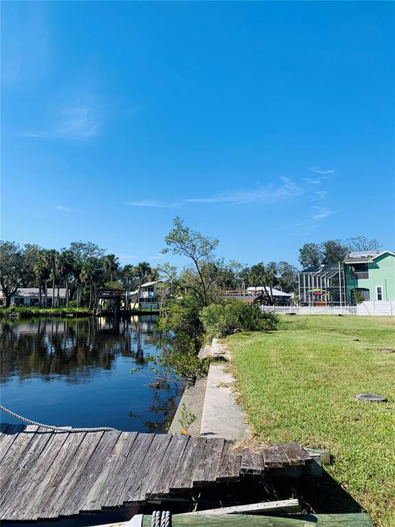 A wooden dock extends into a canal alongside a grassy yard and residential homes — 5948 RIVERSIDE DRIVE, PORT ORANGE, FL