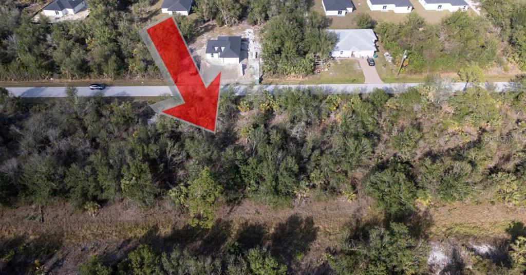 An aerial view shows a wooded, undeveloped lot with a large red arrow pointing down — 7051 LEGION STREET, PORT CHARLOTTE, FL
