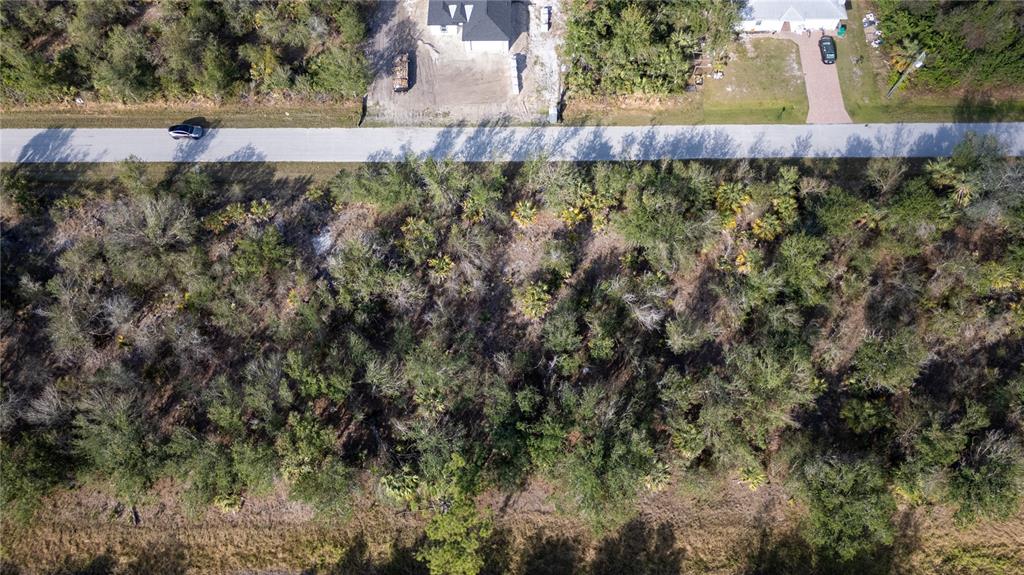 An aerial view shows a wooded lot situated between a paved road and a grassy field — 7051 LEGION STREET, PORT CHARLOTTE, FL