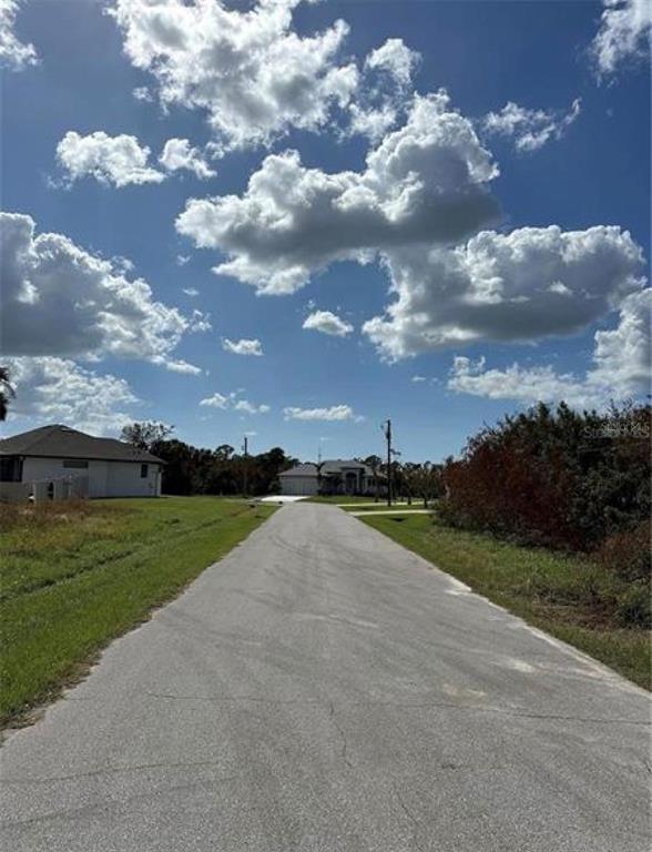 A paved road leads toward a residential house under a blue sky with scattered clouds — 232 SPRING DRIVE, ROTONDA WEST, FL