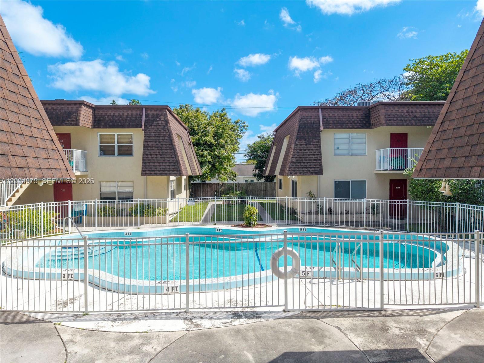 A swimming pool is enclosed by a white metal fence in front of two apartment buildings — 4524 SW 54th St, Dania Beach FL 33314, DANIA BEACH, FL