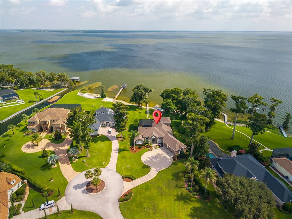 An aerial view shows a large waterfront house with a circular driveway and green lawn — 7311 BIRDS NEST COURT, YALAHA, FL