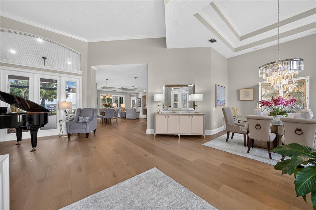 A spacious dining and living area features hardwood floors, a grand piano, and a crystal chandelier — 7311 BIRDS NEST COURT, YALAHA, FL