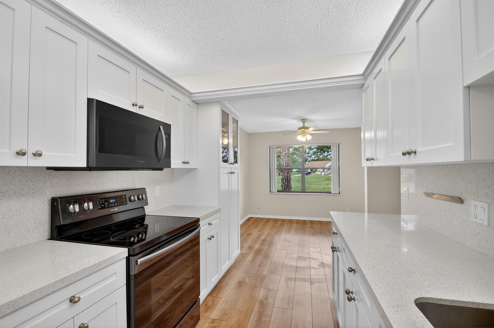 A kitchen with white cabinets, quartz countertops, and black appliances opens to a dining area — 6105 Fairfield Circle, FL 33463, FL