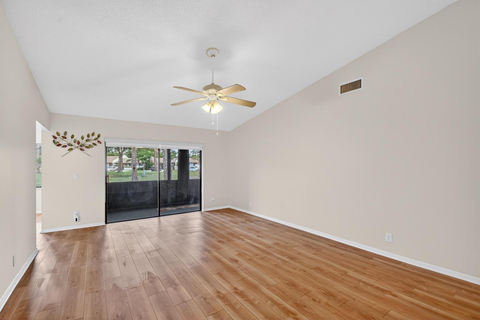 An empty living room features wood-look flooring, a vaulted ceiling with a fan, and sliding doors — 6105 Fairfield Circle, FL 33463, FL