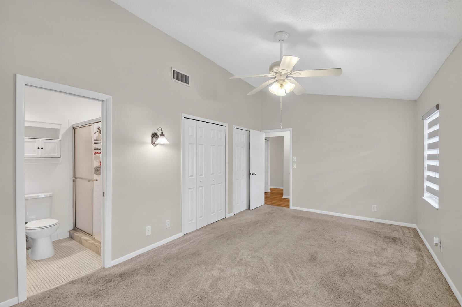 A carpeted bedroom with a ceiling fan, vaulted ceiling, and an attached bathroom — 6105 Fairfield Circle, FL 33463, FL