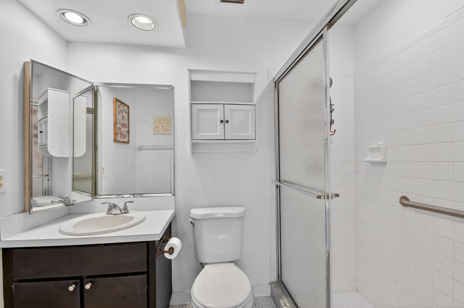 A bathroom features a dark vanity, a toilet, a shower stall, and a wall-mounted cabinet — 6105 Fairfield Circle, FL 33463, FL