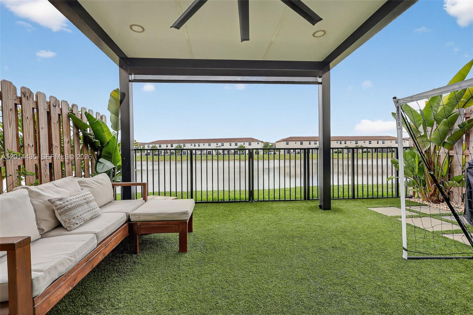 A covered patio features artificial turf, a wooden sofa, and a black fence overlooking water — 12808 NW 22nd Pl, Miami FL 33167, MIAMI, FL