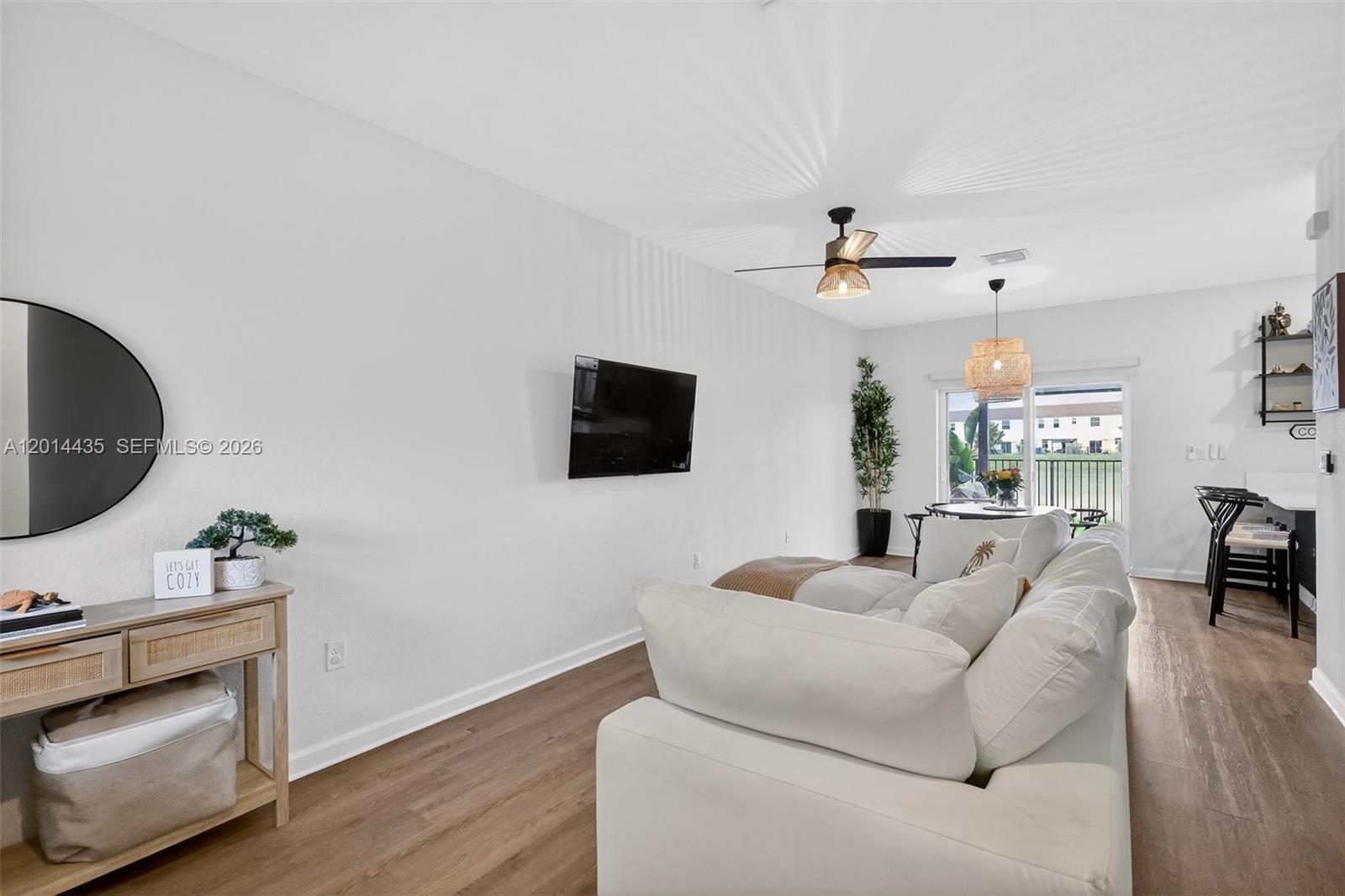 A living room features a white sofa, wall-mounted television, and wood-look flooring — 12808 NW 22nd Pl, Miami FL 33167, MIAMI, FL