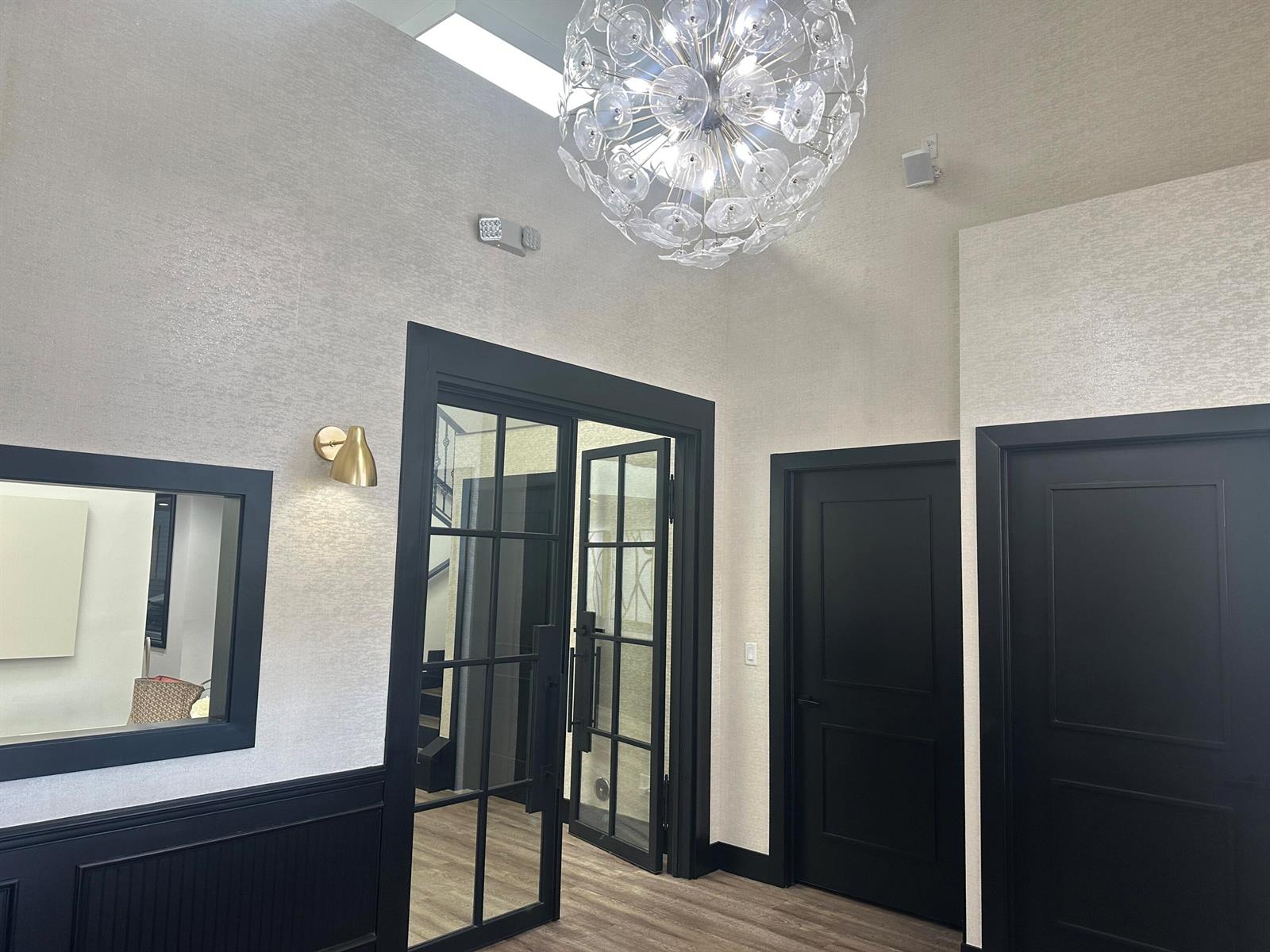 A modern interior hallway features black-framed doors, a textured wall, and a large spherical chandelier — 900 E Atlantic Avenue # 12, Delray Beach FL 33483, DELRAY BEACH, FL
